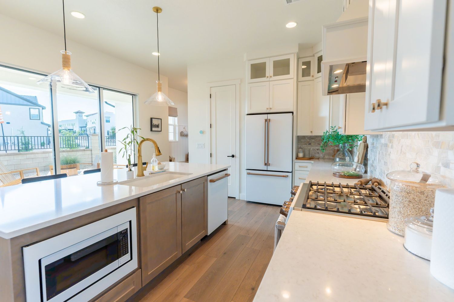 Modern white kitchen with quartz countertops, pendant lights, stainless appliances, and hardwood floors in an open layout.