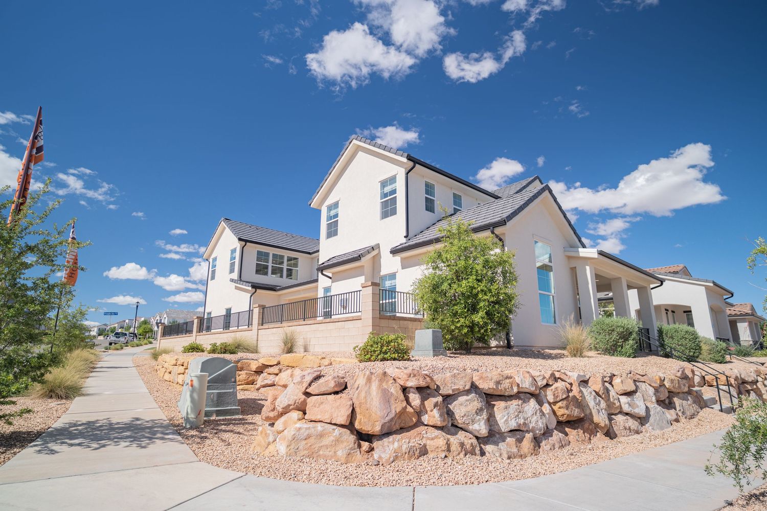 Modern two-story white home with stone landscaping, blue front door, and desert xeriscape under a bright blue sky.