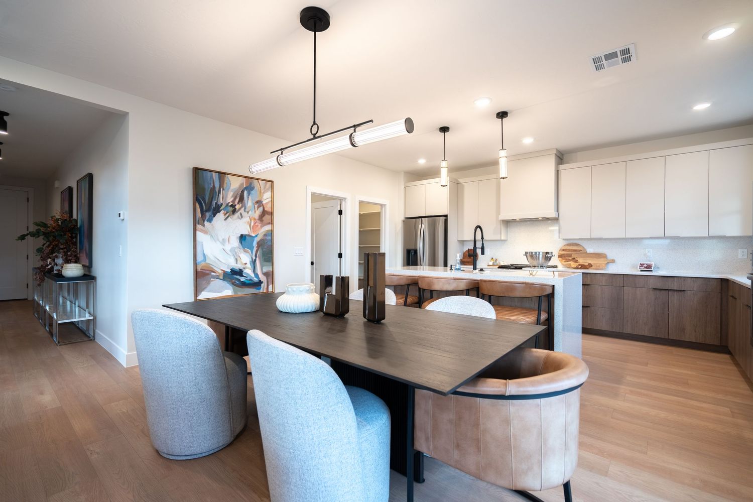 Modern open concept kitchen with white cabinets, wood floors, and pendant lighting showcases sleek minimalist design.