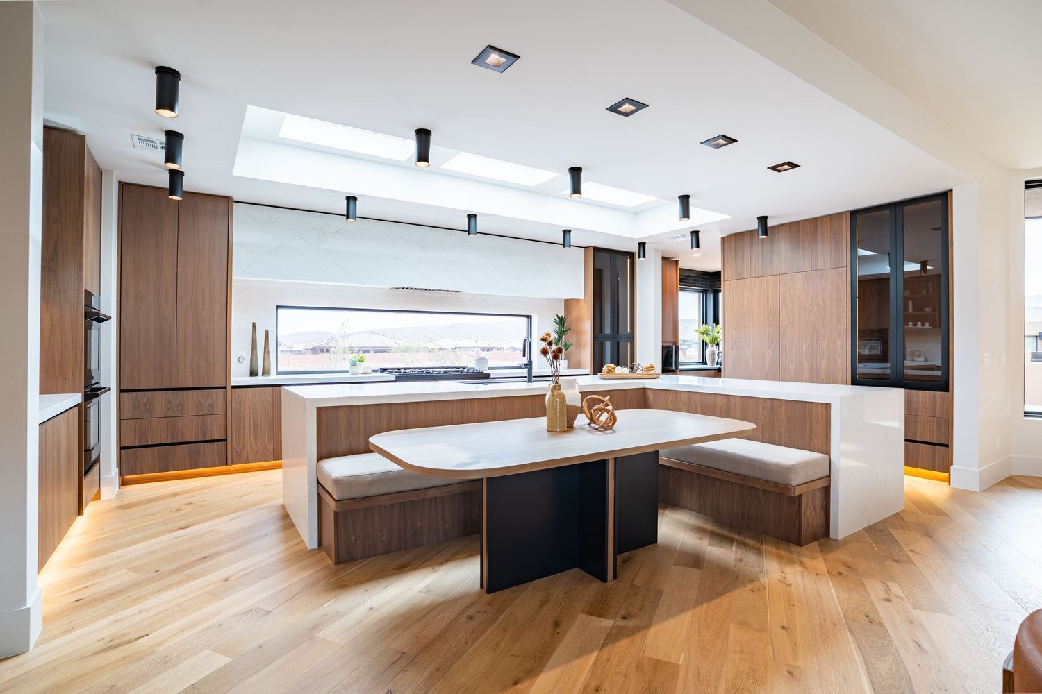 Modern luxury kitchen with wooden floors, built-in bench seating, and white quartz waterfall island in an open concept space.