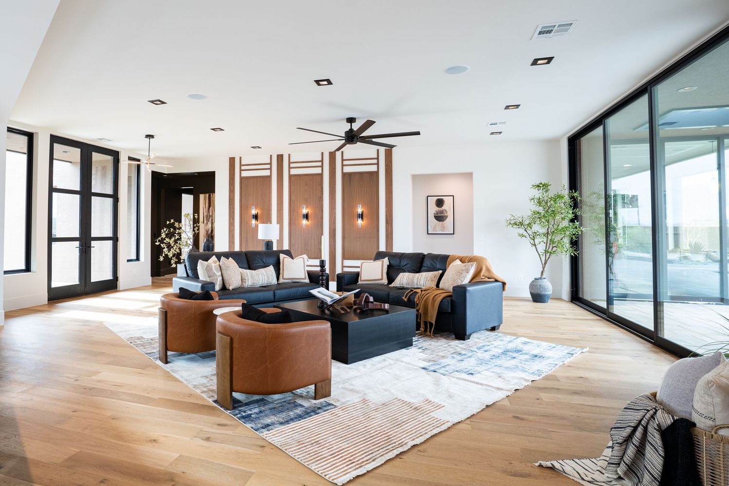 Modern open concept living room features wood floors, large windows, and brown leather furniture with minimalist decor.
