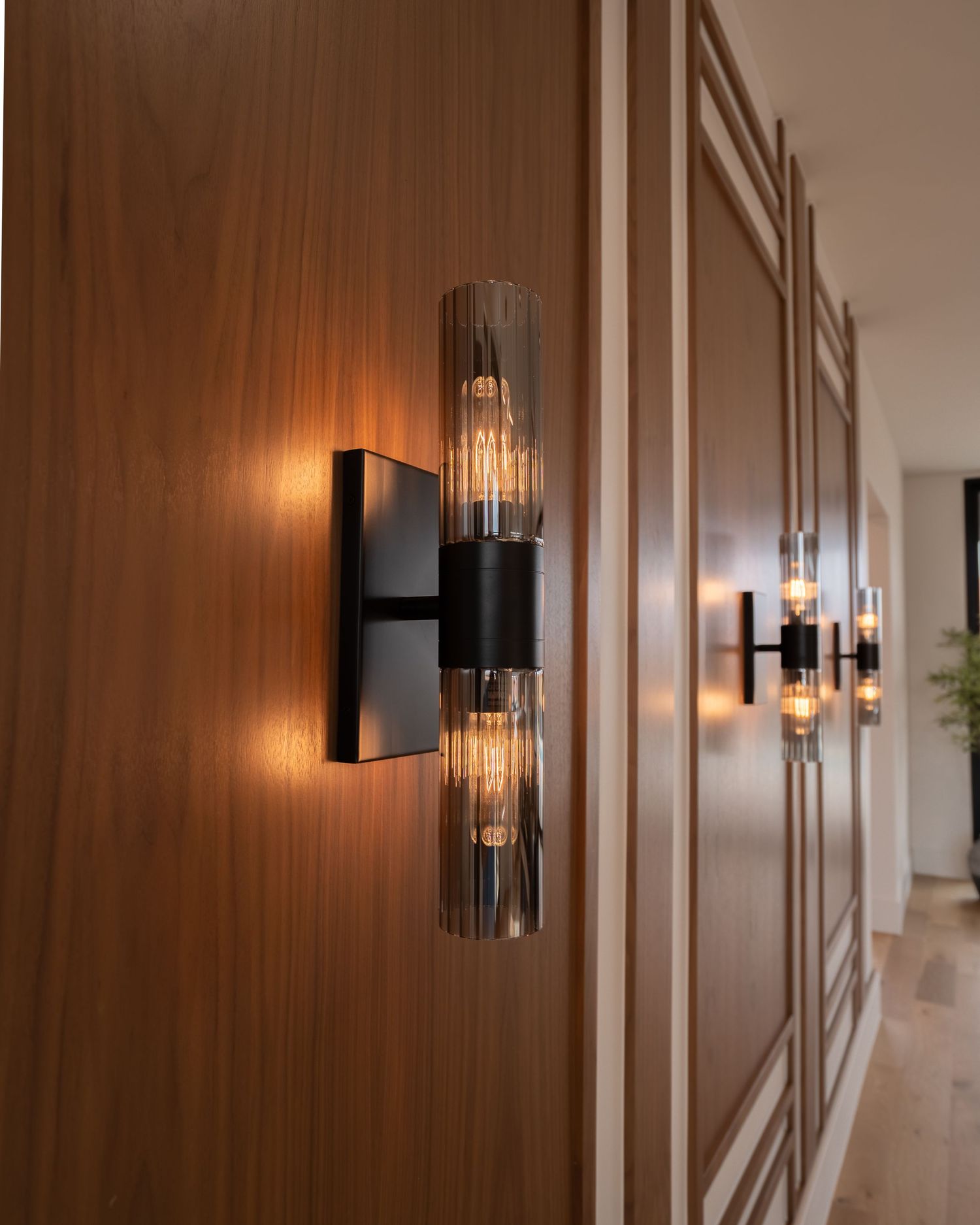 Modern hallway with wood paneling and elegant glass wall sconces creating warm ambient lighting.