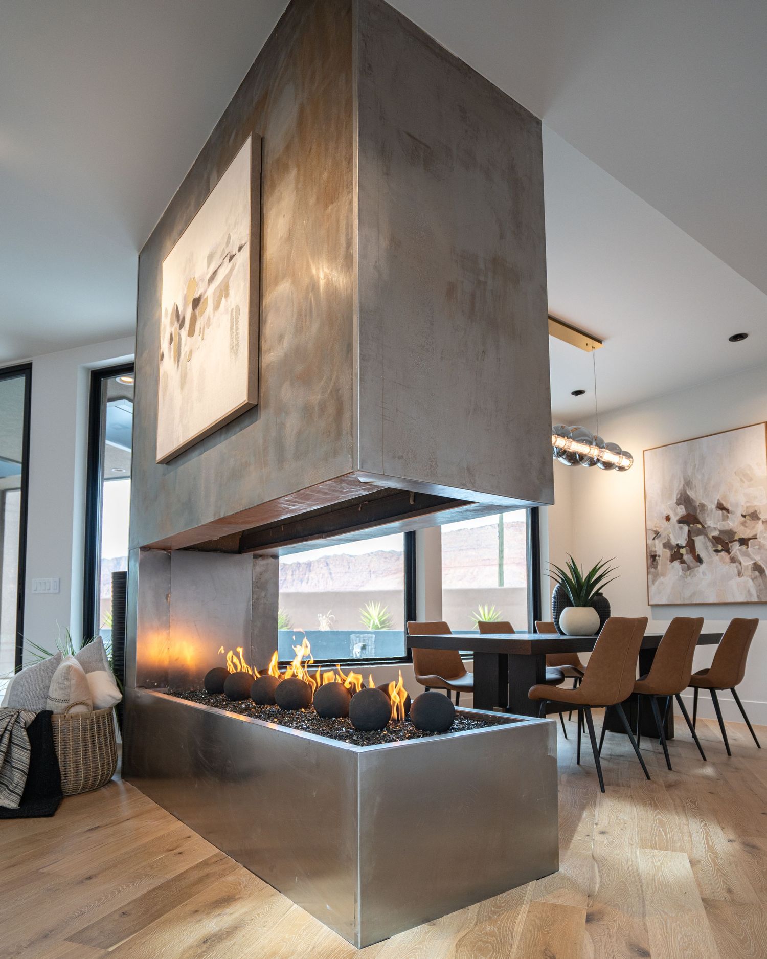 Modern living room features a striking suspended metal fireplace with glass enclosure and light hardwood floors.