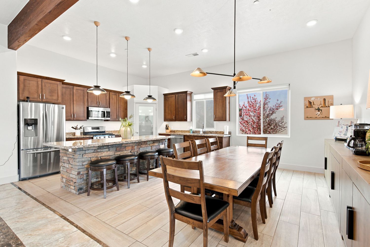 Spacious open-concept kitchen and dining area with dark wood cabinets, stone island, stainless appliances, and farmhouse dining table.
