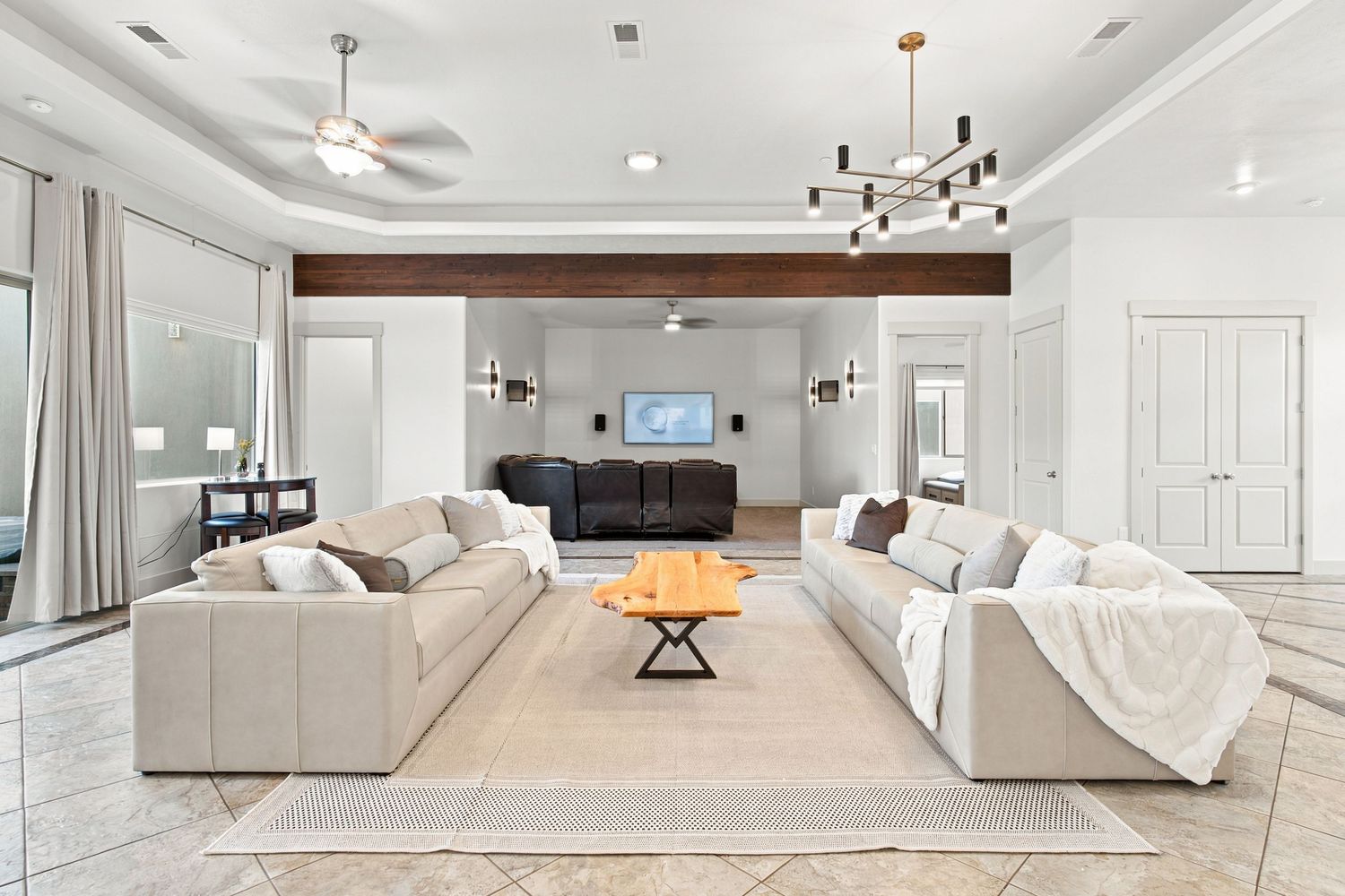 Spacious open-concept living room with white sectional sofas, tray ceiling, dual ceiling fans, and modern chandelier lighting.