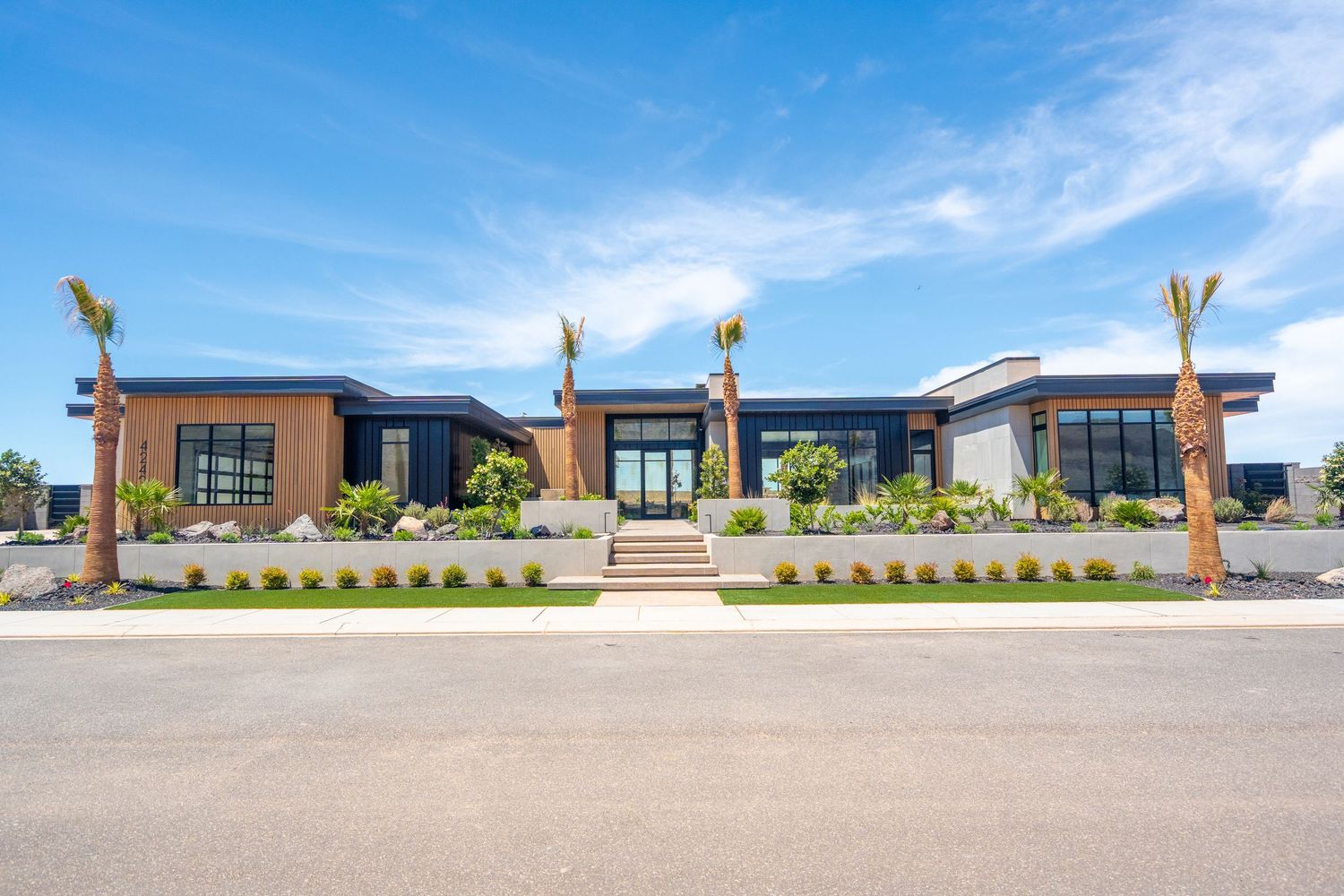 Modern single-story luxury home in St George, Ut with dark exterior, large windows, and desert landscaping under blue sky.