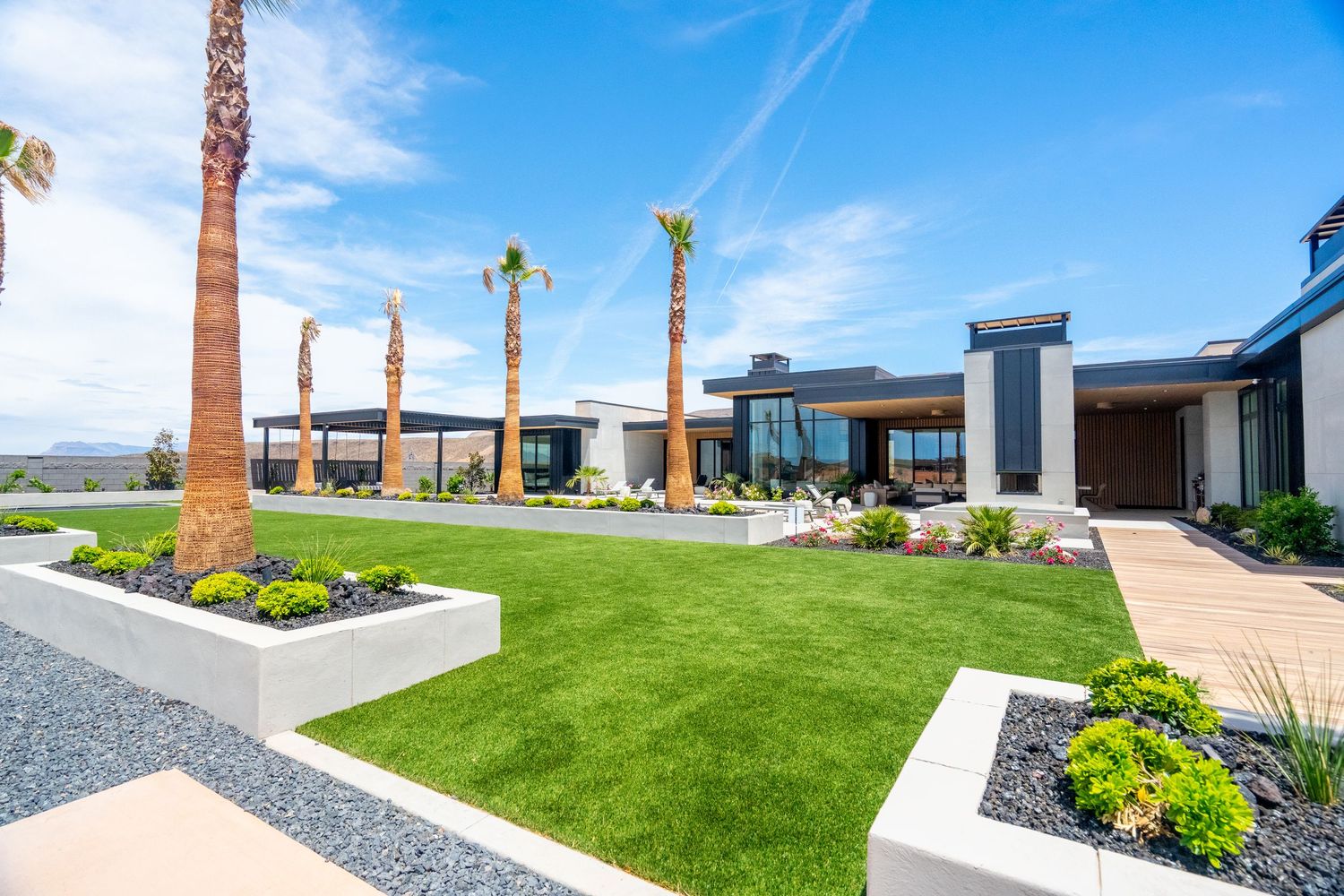 Modern desert home in St George, Ut. Exterior with manicured lawn, palm trees and contemporary landscaping under bright blue sky.