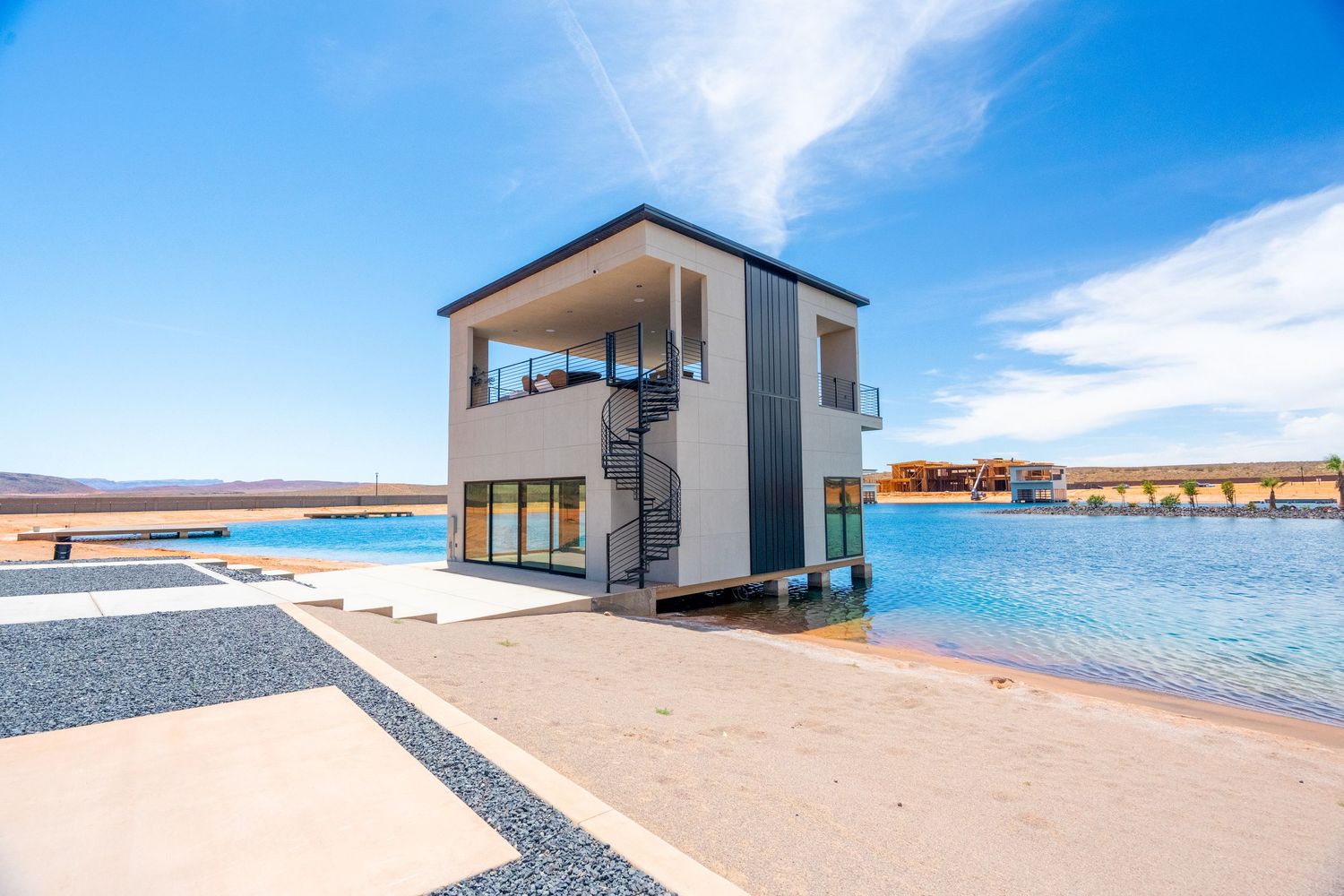 Modern beach house in St George, Ut with large windows overlooks calm blue waters on a sunny day.