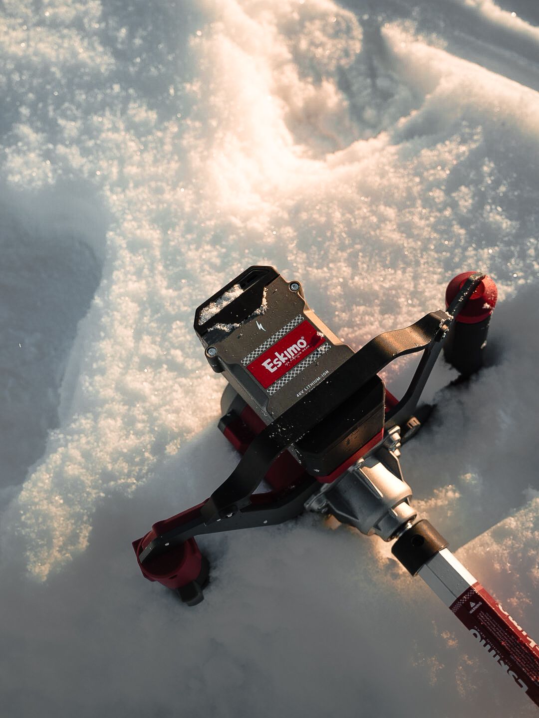 Overhead view of red ice auger drill head in fresh snow.