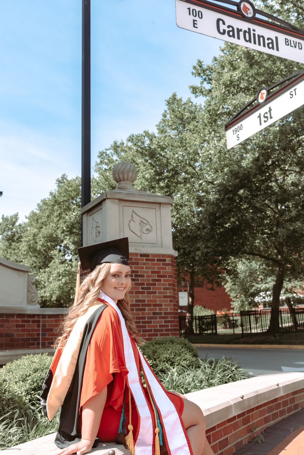 Graduate in red stole poses near Cardinal Boulevard street sign.