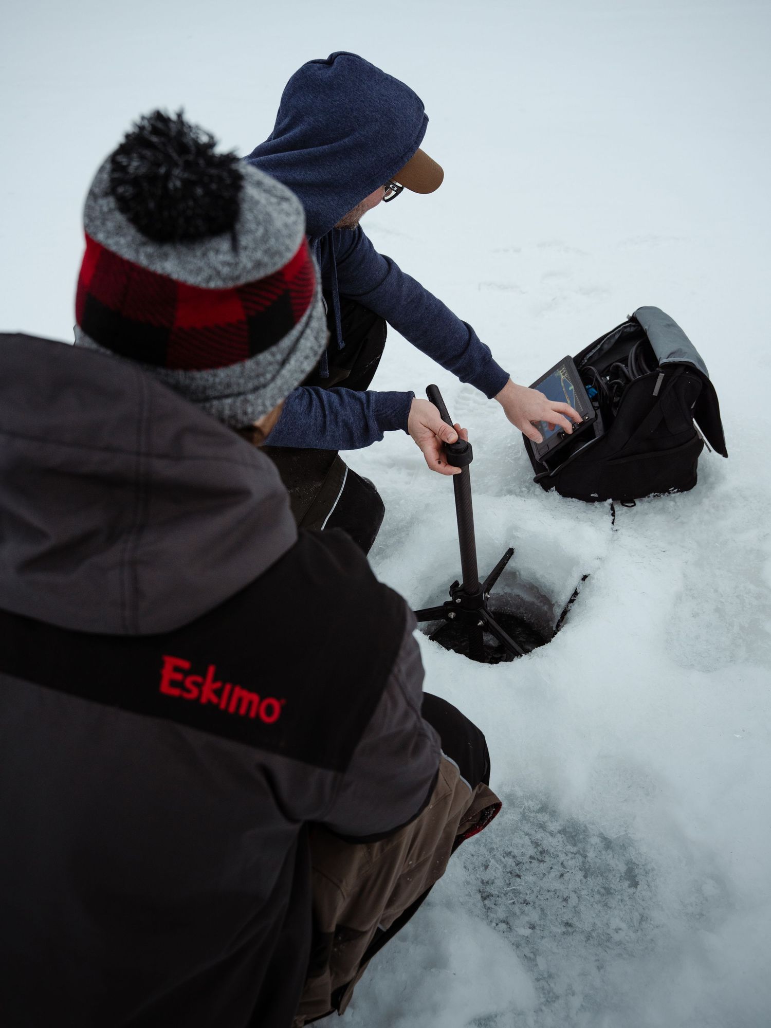 Ice fisherman drilling a hole in frozen lake with manual auger while wearing winter gear.