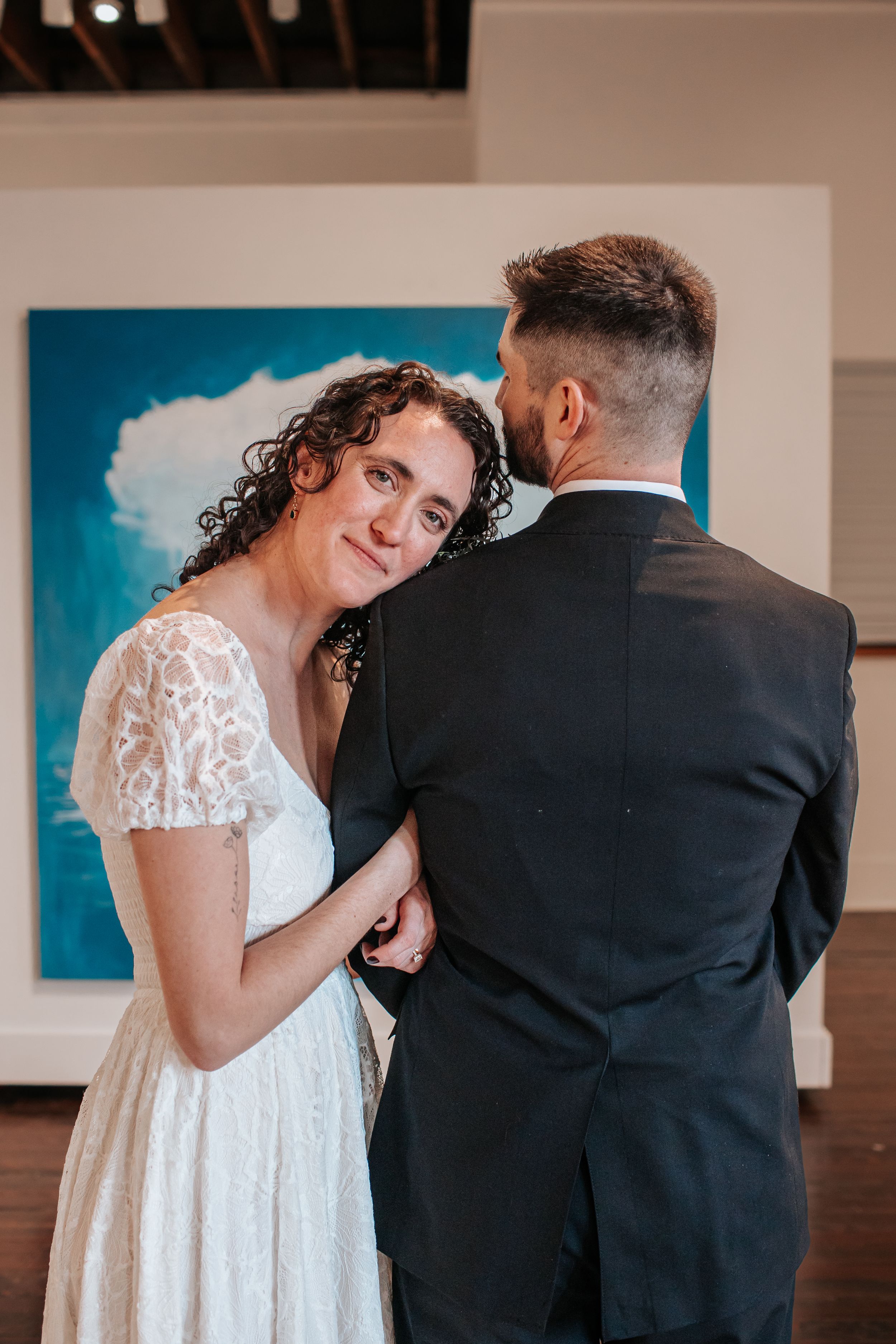 A tender moment between a bride in a lace dress and someone in a dark suit during a wedding dance.