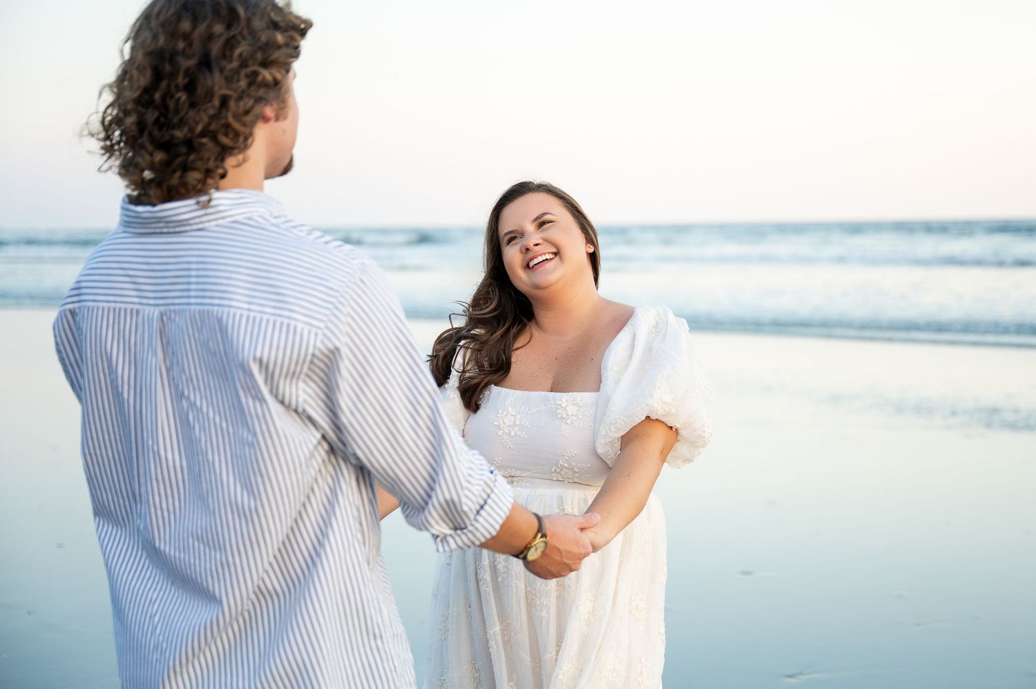 A couple holds hands and dances together on a peaceful beach at dusk.