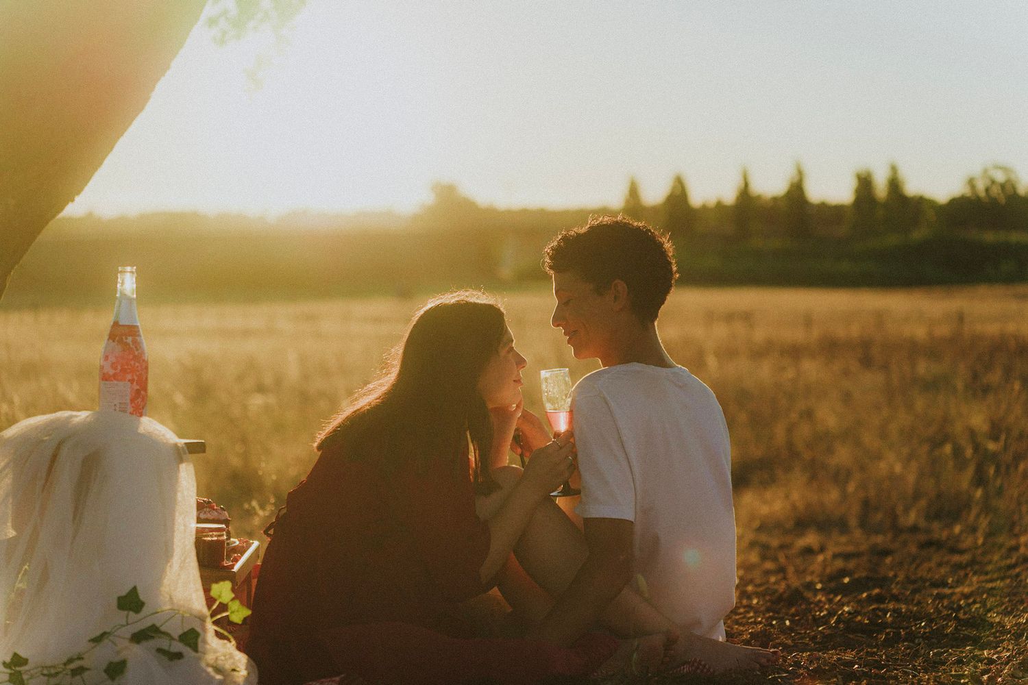 Children playing near a large oak tree with a tire swing in a sunny golden field at sunset.