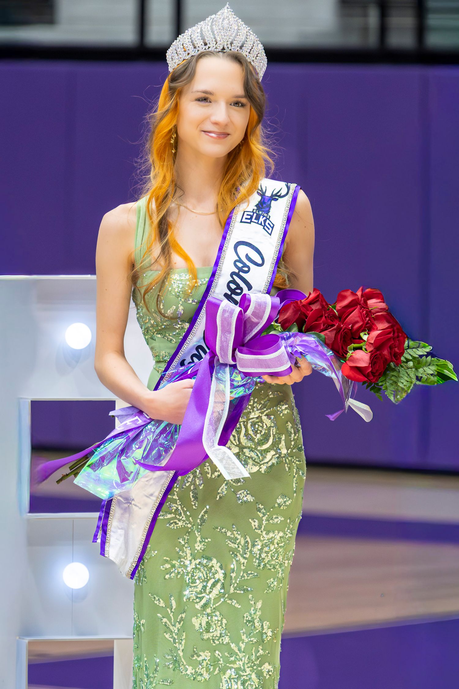A pageant winner in a green dress stands next to a basketball player wearing an Elkins Basketball uniform.