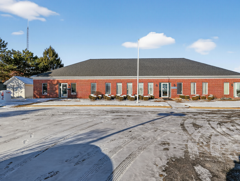 Brick commercial building with hip roof, flagpole, and snow-covered parking lot.
