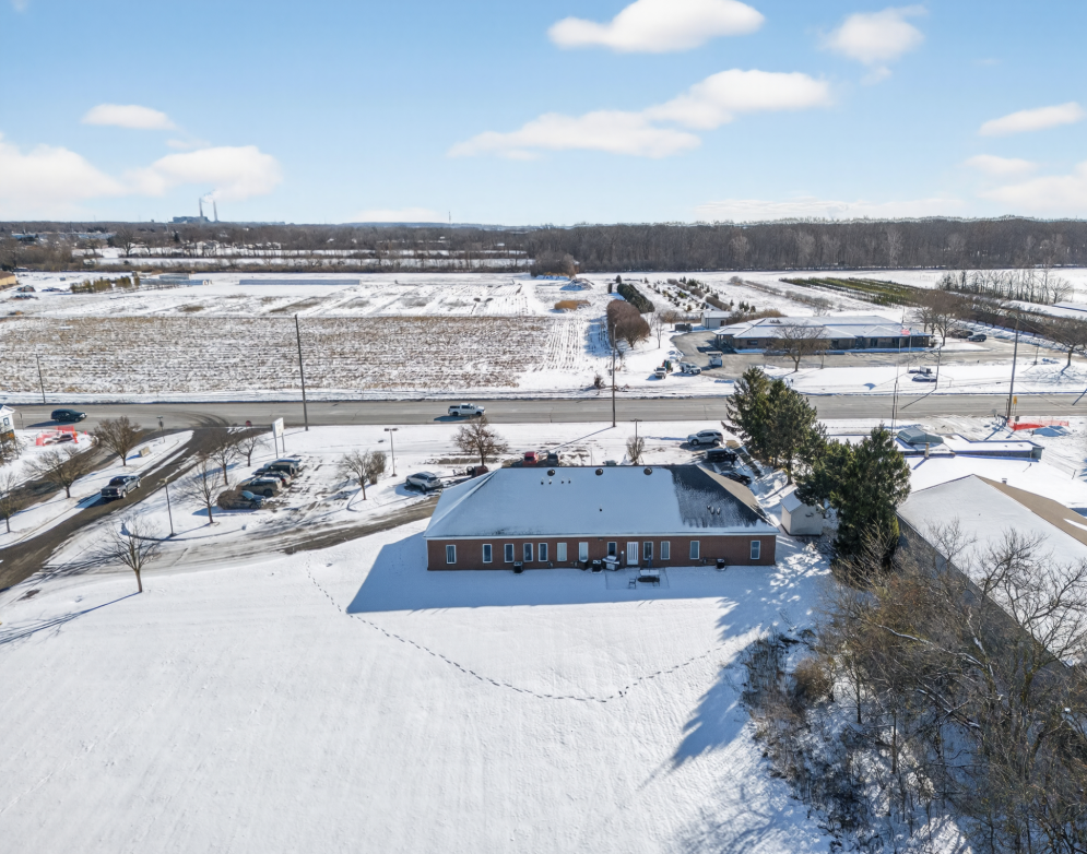 Aerial view of snow-covered commercial property near a busy road and open fields.