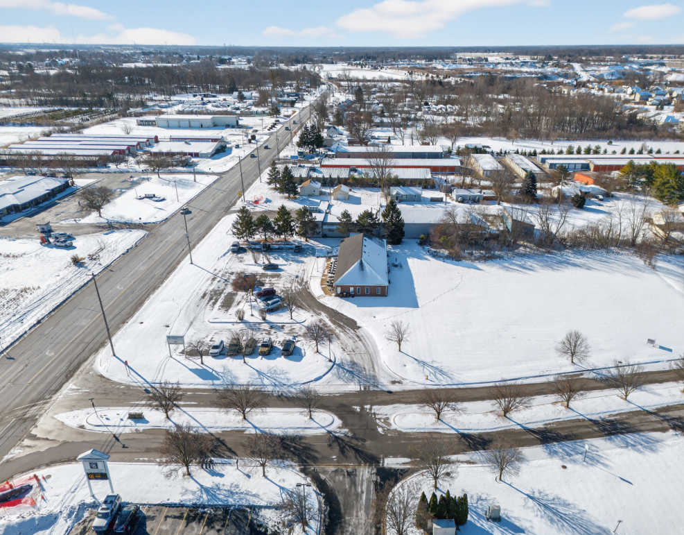 Aerial winter view of a small brick building at a snowy intersection surrounded by suburban commercial development.
