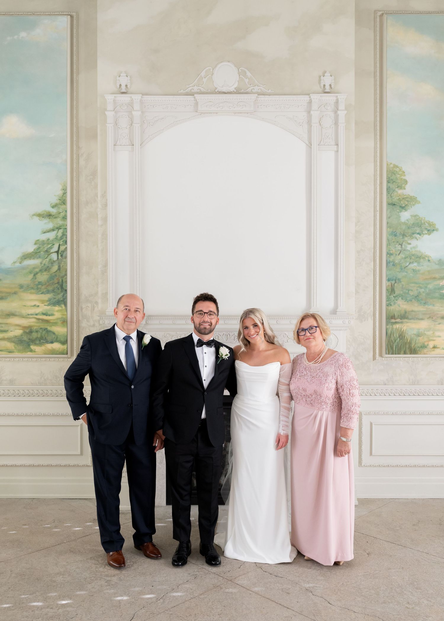 A wedding party poses in an elegant white room with painted landscape murals on the walls.