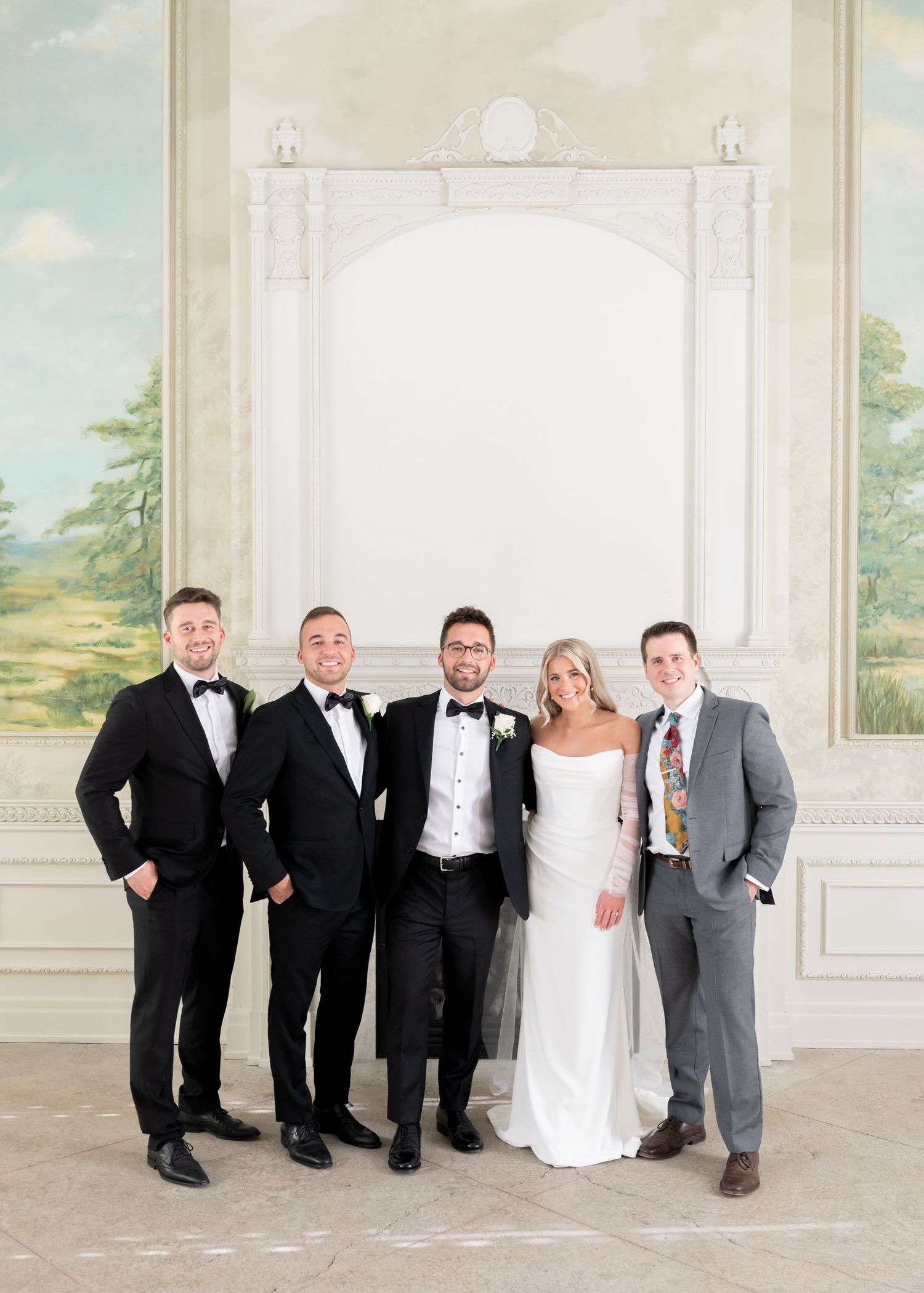 Wedding party poses playfully while lying on the floor in an elegant room with landscape murals.