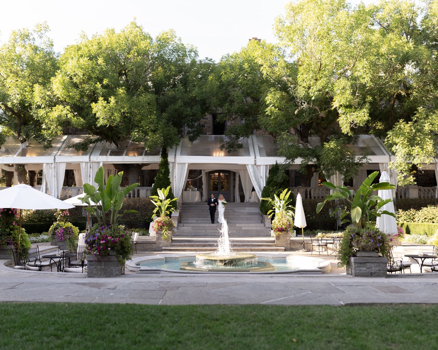 Panoramic view of an elegant outdoor event space with white curtains, pool, and lush garden landscaping in golden sunlight.