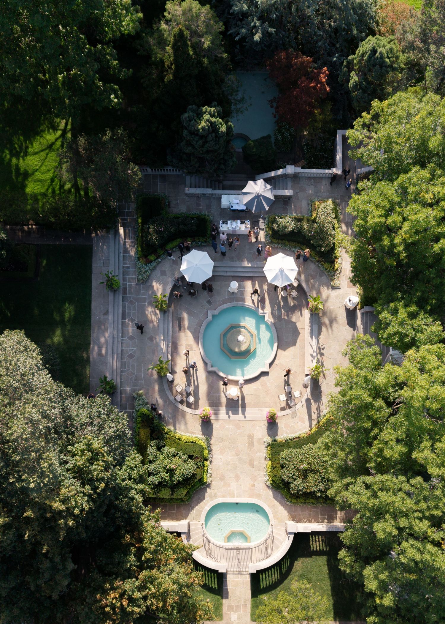 Aerial view of a luxurious backyard swimming pool with circular design elements surrounded by lush green trees.