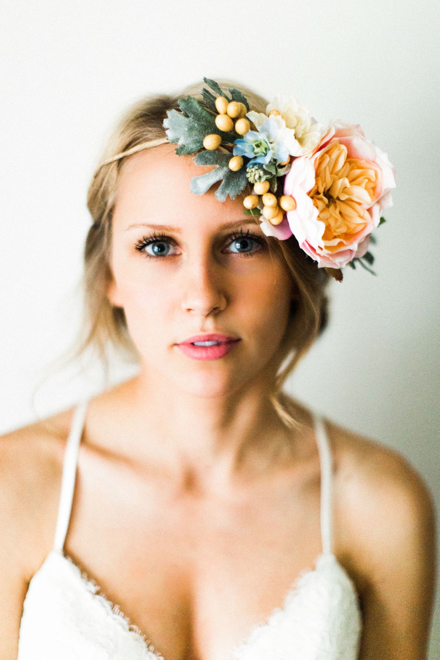 Soft portrait with peach and blue floral crown against white background.