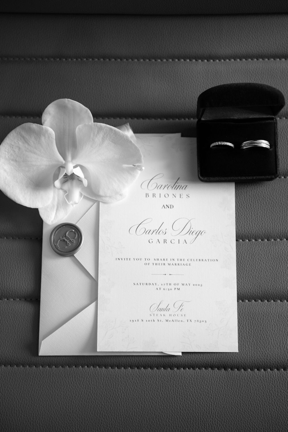 Black and white wedding invitation suite with elegant calligraphy and white orchid flowers displayed on a leather surface.