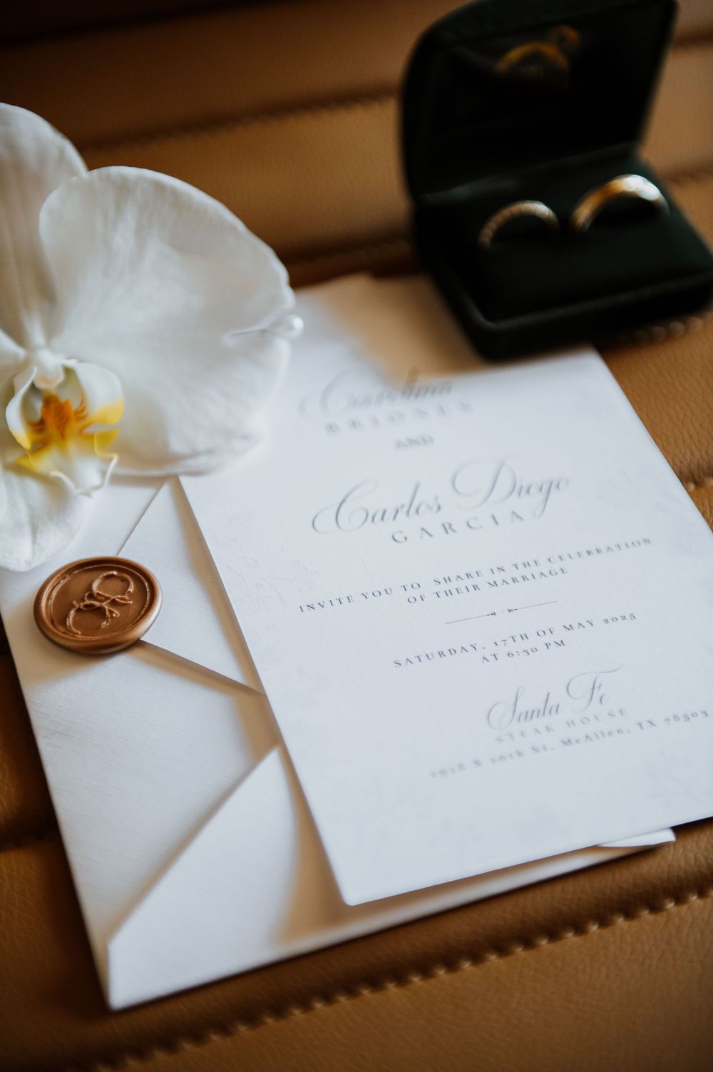 Elegant white wedding invitations with calligraphy lettering displayed with delicate white orchid petals on brown surface.