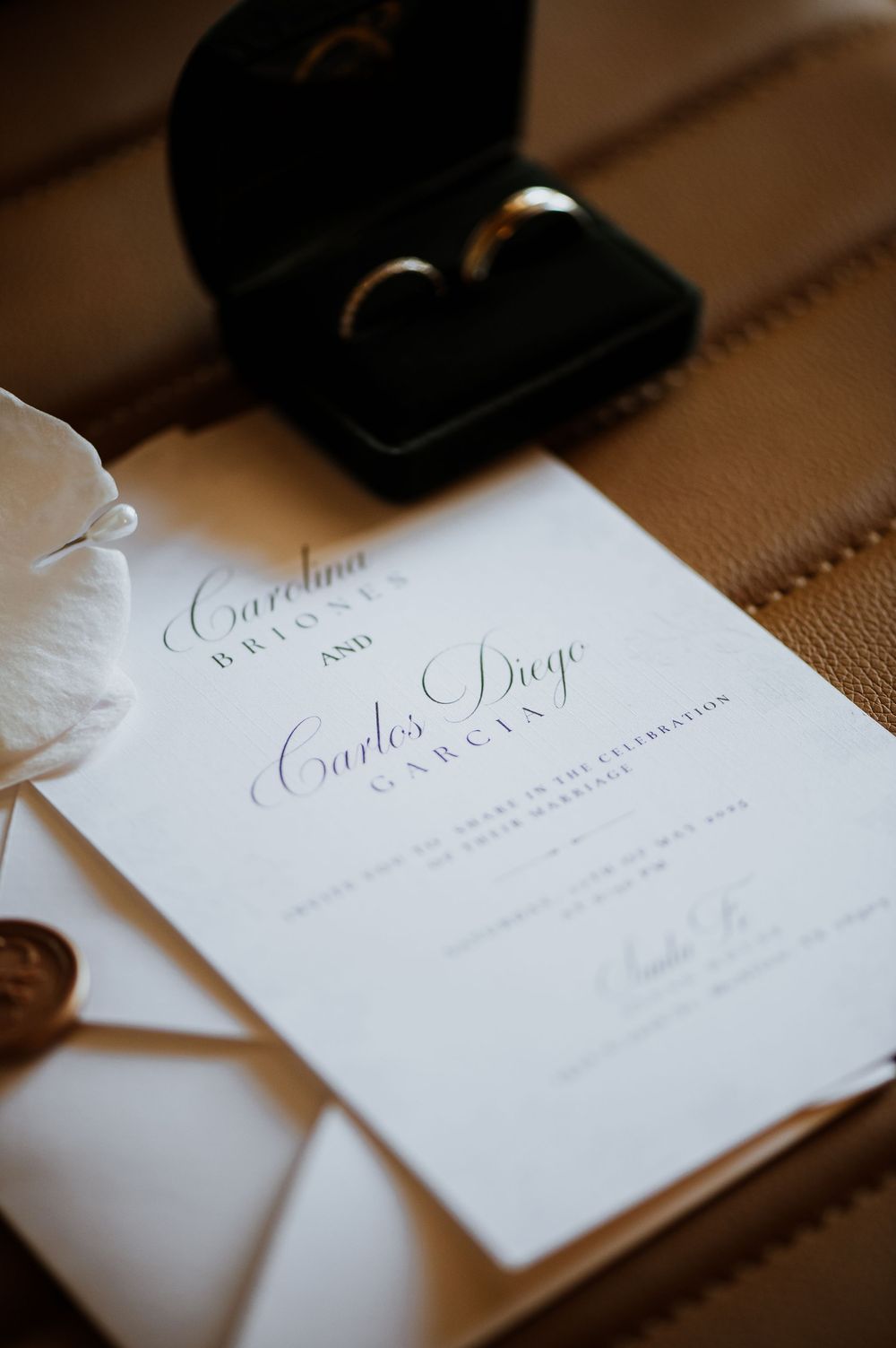 Elegant wedding invitation with calligraphy text and wedding rings in black box on brown leather surface.