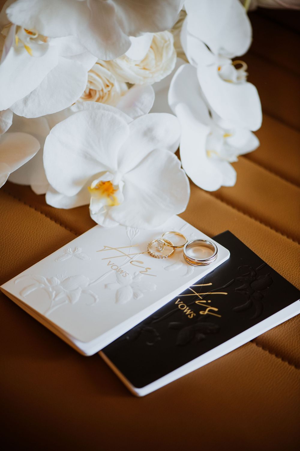 Wedding rings rest elegantly against a black and white surface with delicate white orchid flowers in the background.