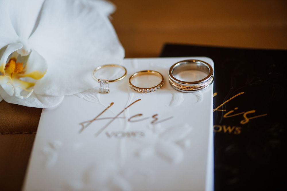 Wedding rings and floral decor displayed on elegant white paper with calligraphy text in romantic lighting.