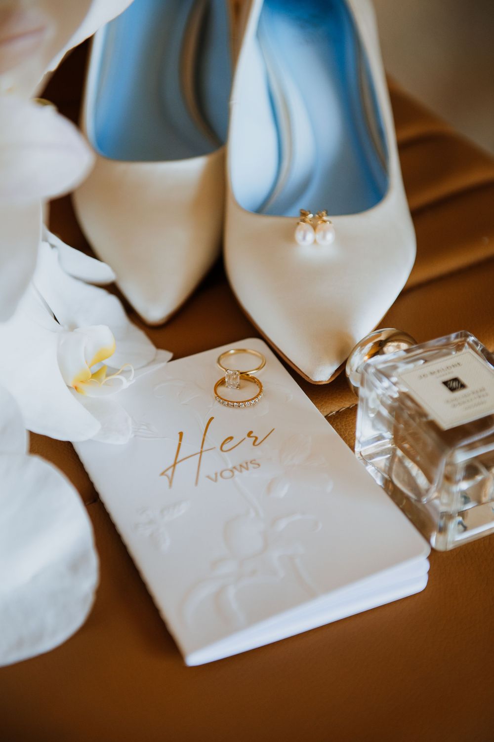 Wedding rings and gold text on white paper with orchid flowers in soft focus.