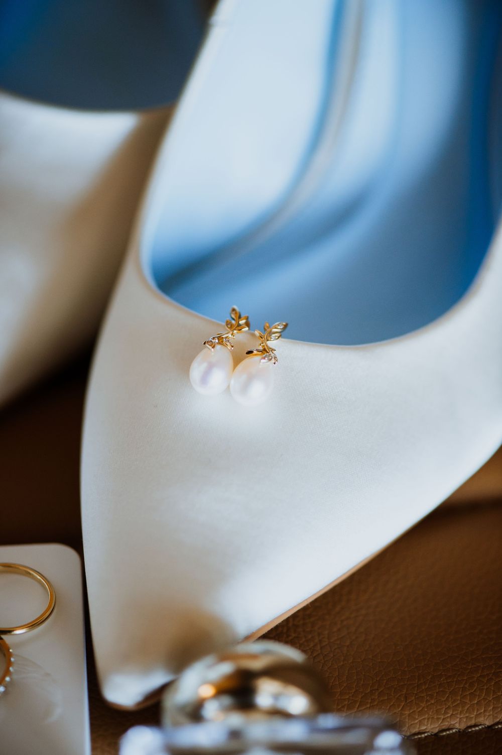 White bridal shoe with delicate gold jewelry detail against a brown background.