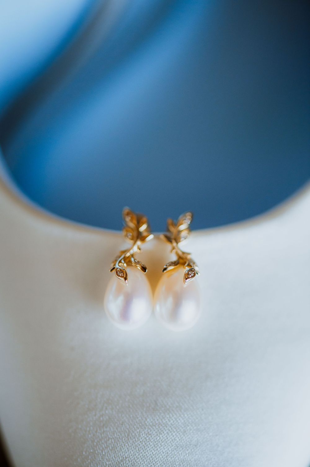 Elegant pearl drop earrings with gold floral accents and crystal details displayed on a white surface.