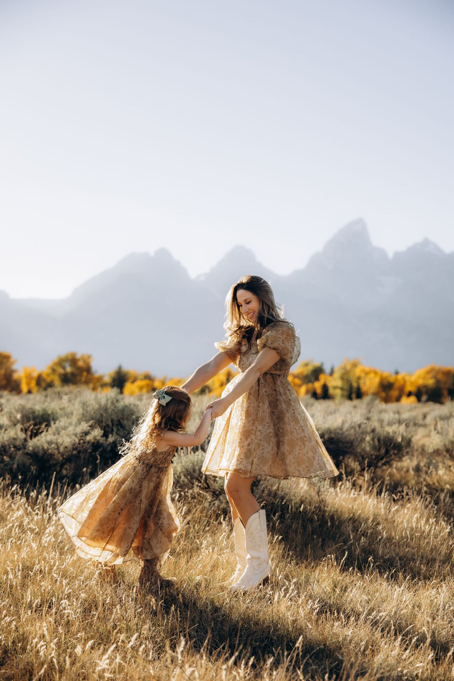 A woman in a flowing white dress runs through a golden field at sunset with mountains in the background.