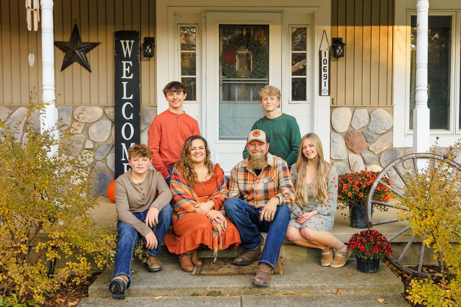 A group sits casually on the steps of a front porch with autumn foliage visible in the foreground.