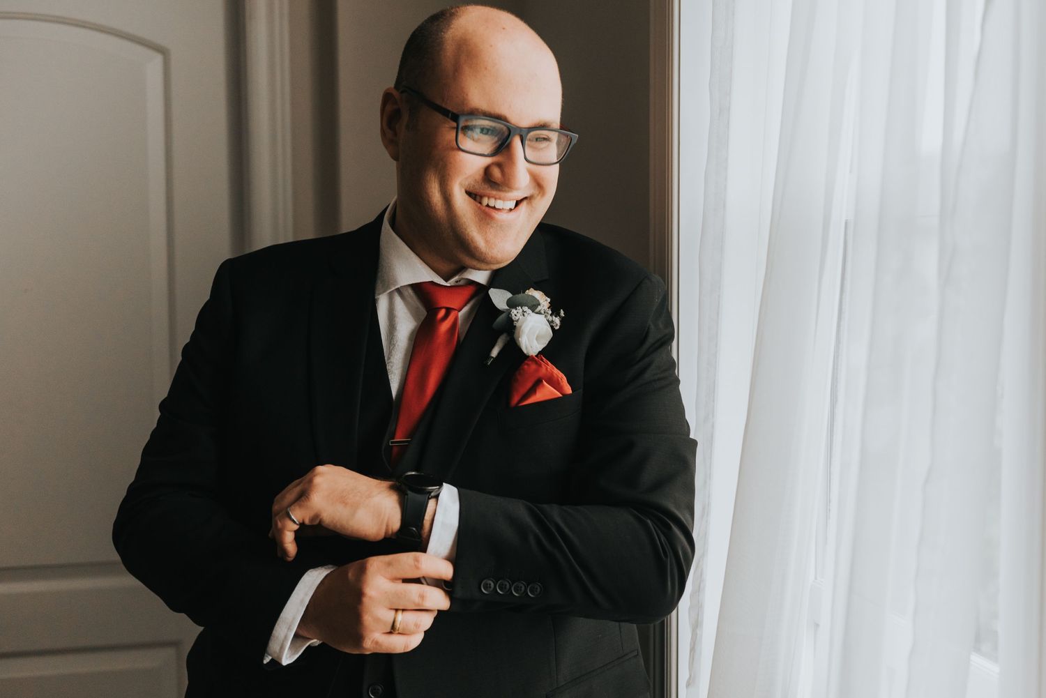 A person in a black suit and red tie smiles while posing for a professional portrait series.