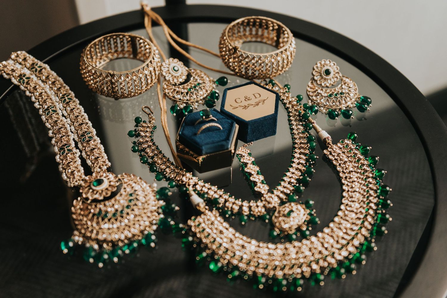 Elegant Indian bridal jewelry set with green emeralds and pearls displayed on black tray with ring box.