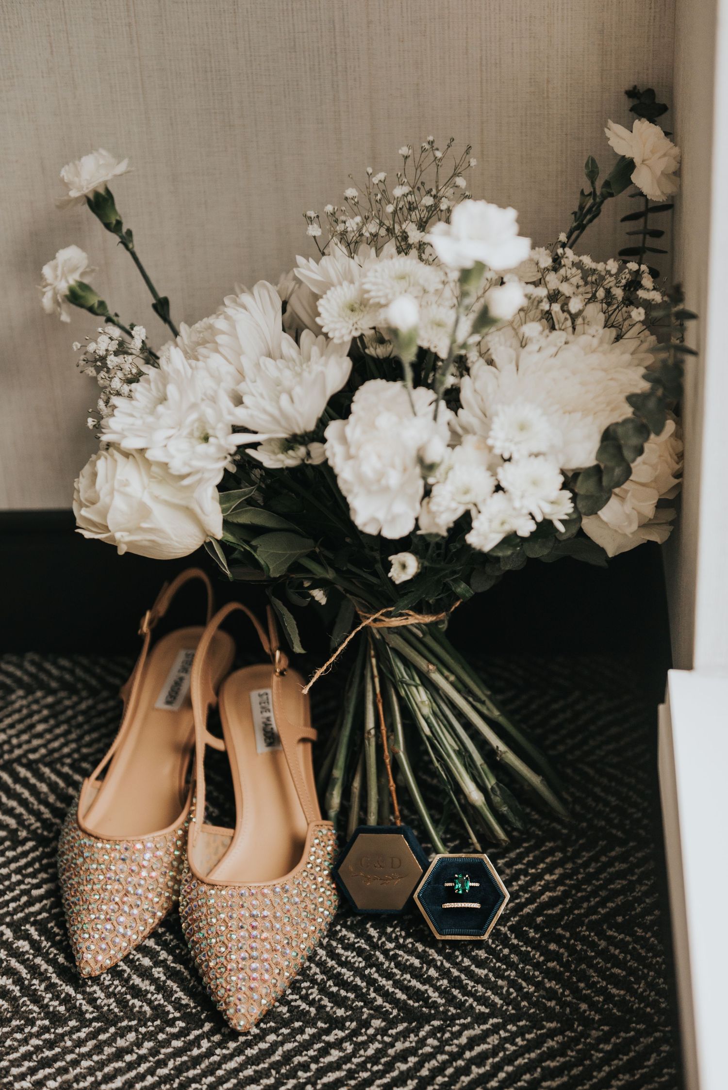 Elegant beige studded bridal shoes displayed with white floral bouquets against a black and white patterned rug.