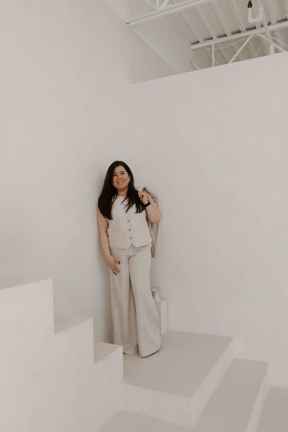 Woman in beige outfit poses playfully on white stairs.