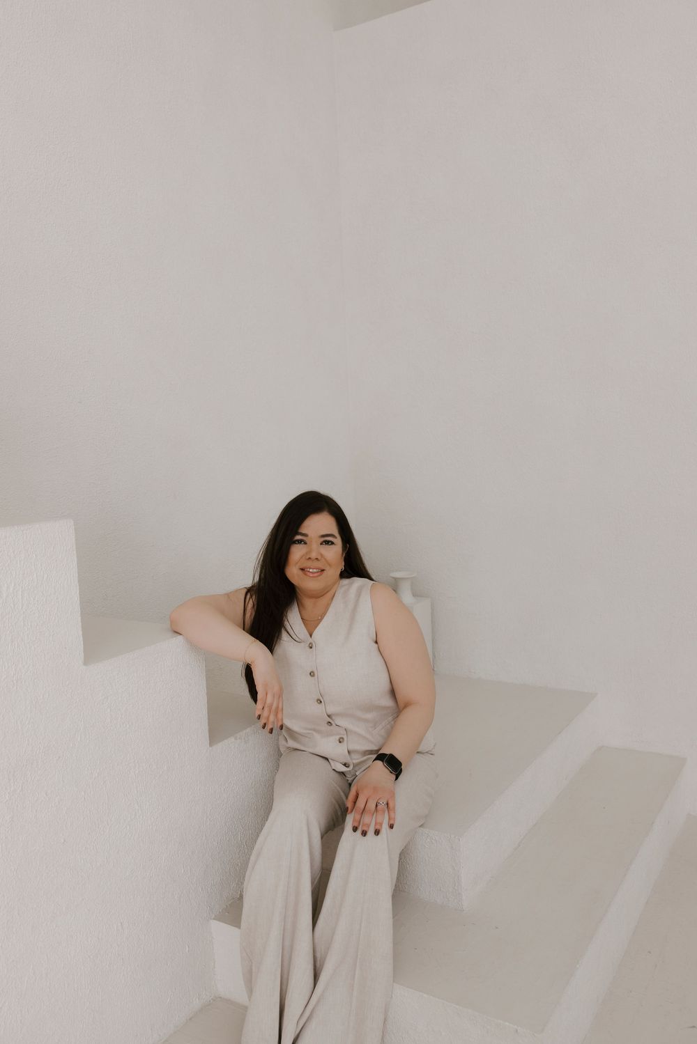 Woman in light neutral outfit sits casually on white stairs.