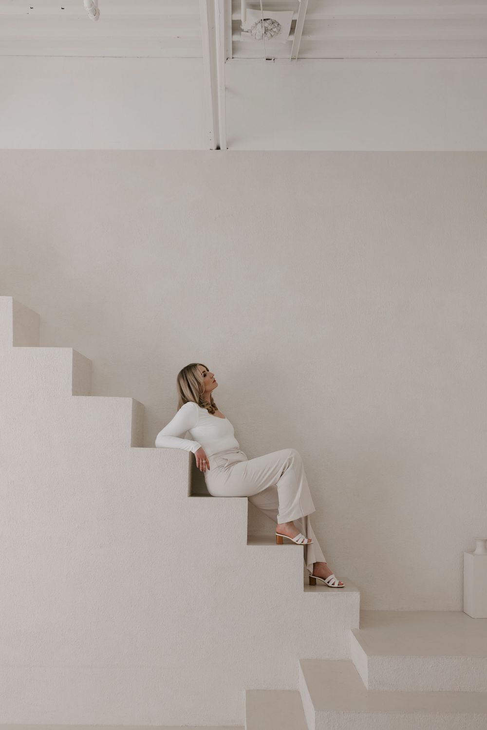 Person wearing light colored outfit poses on geometric white architectural steps.