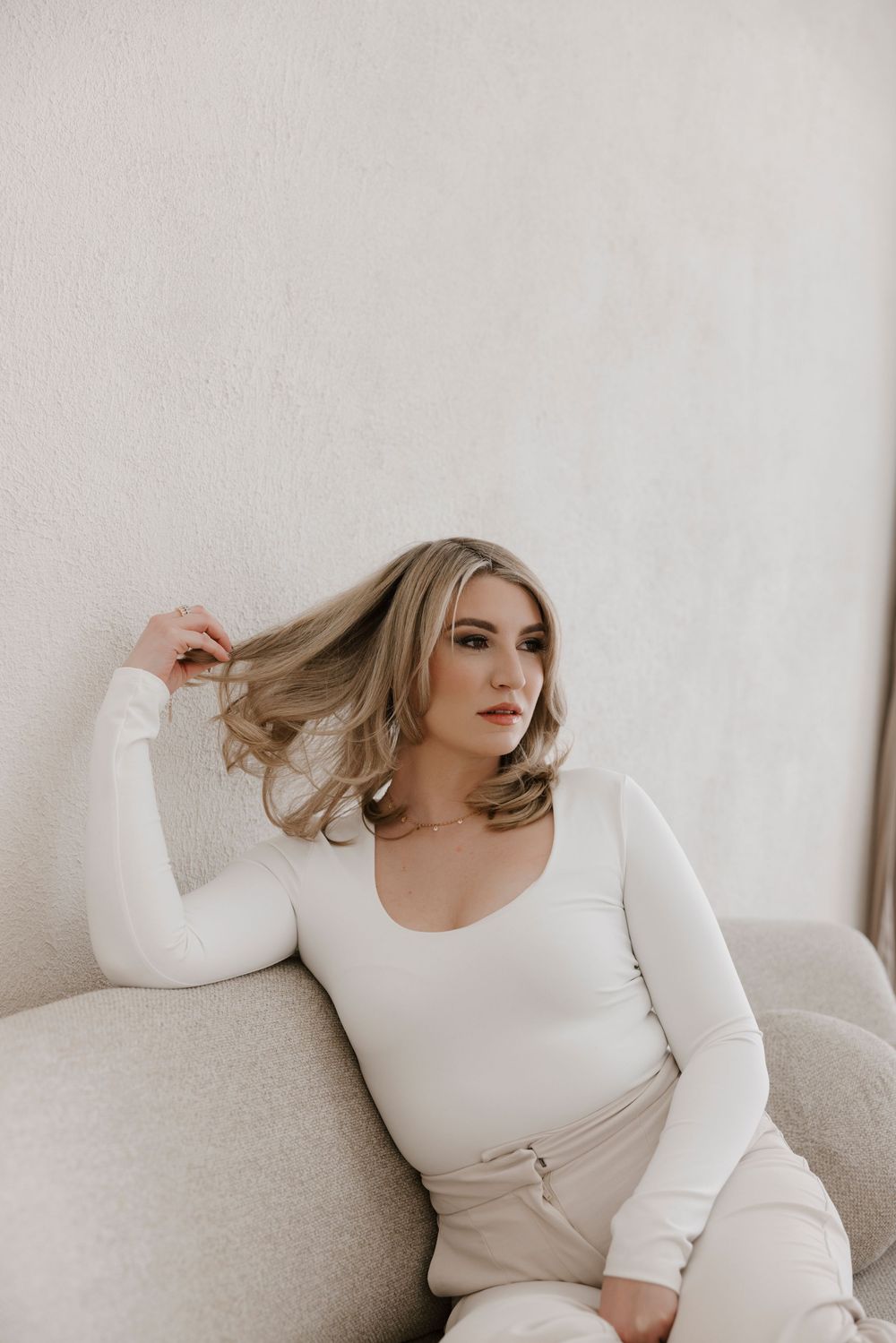 Woman in white loungewear poses on light-colored couch.