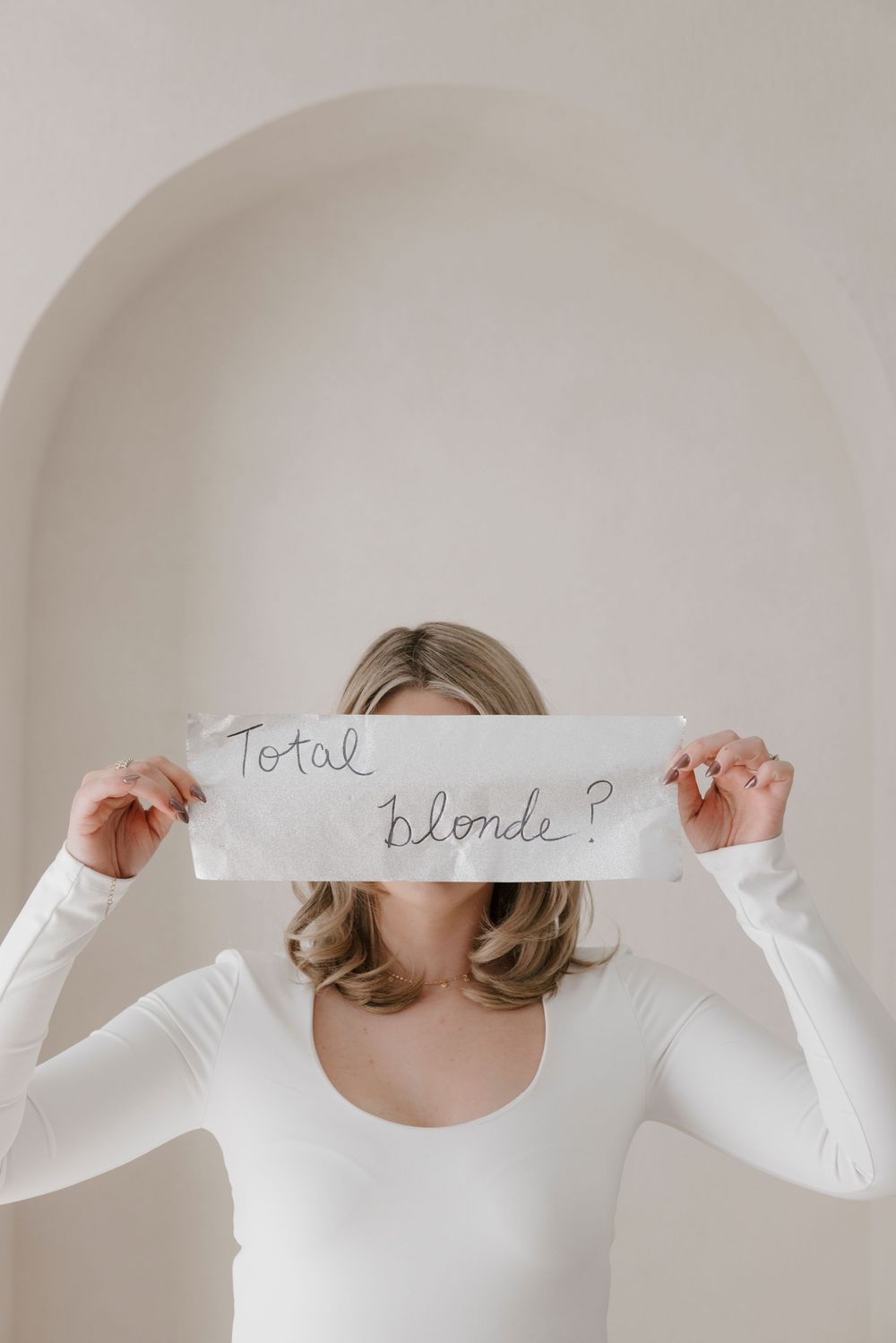 Minimalist fashion photoshoot featuring a white sweater against neutral background with text on paper.