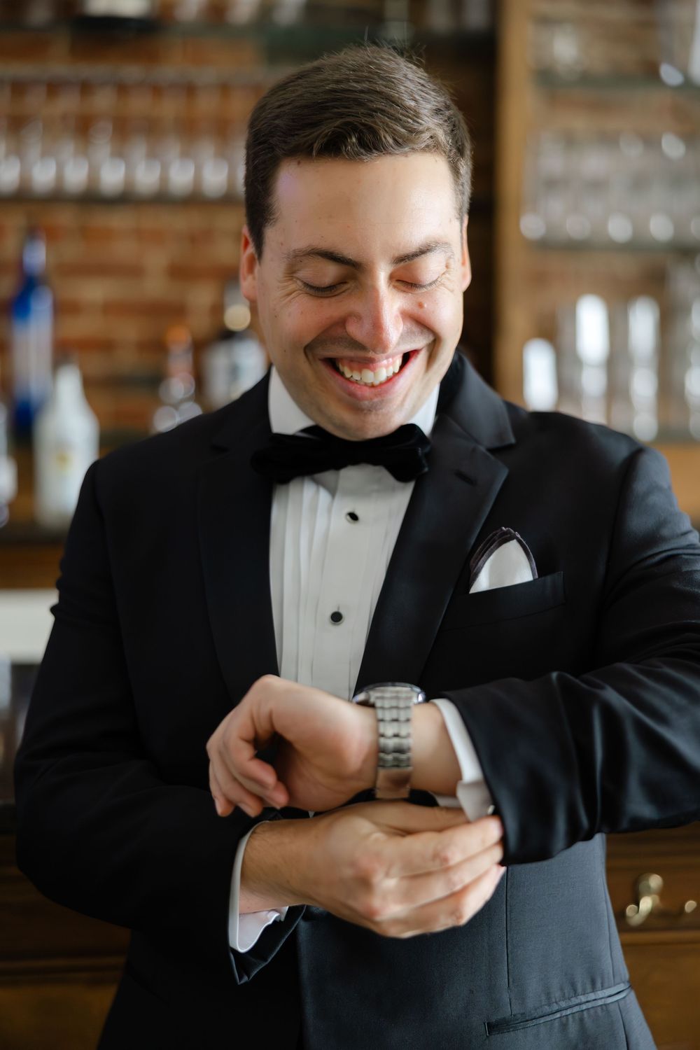 Person in tuxedo smiles while looking down at smartphone screen in a restaurant setting.