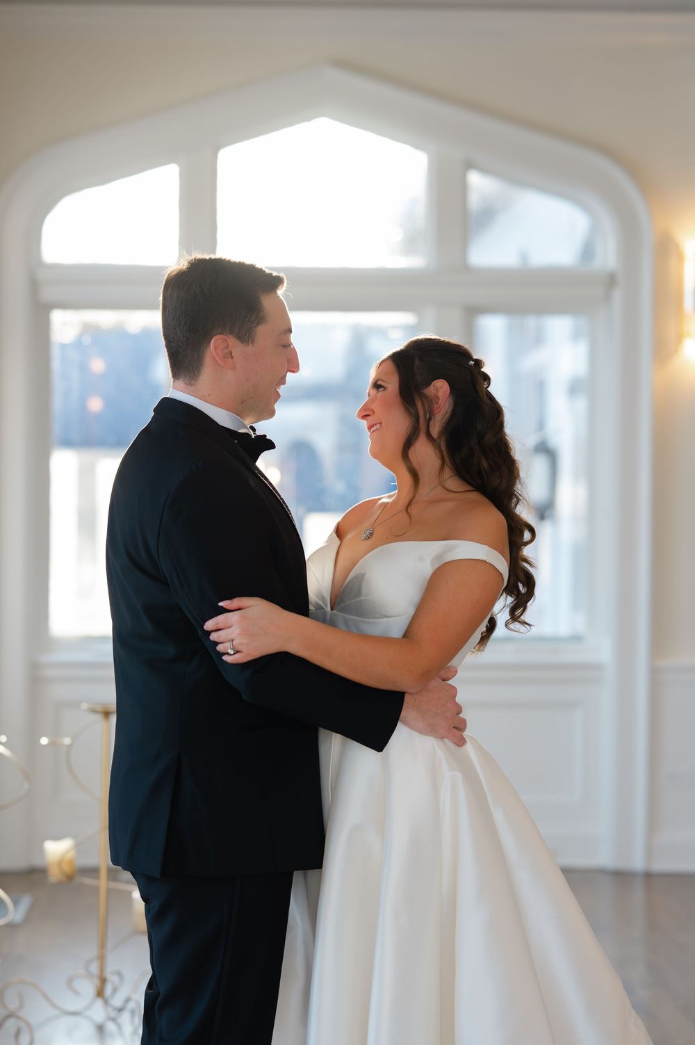 A romantic first dance between newlyweds in a bright, sunlit room with arched windows.