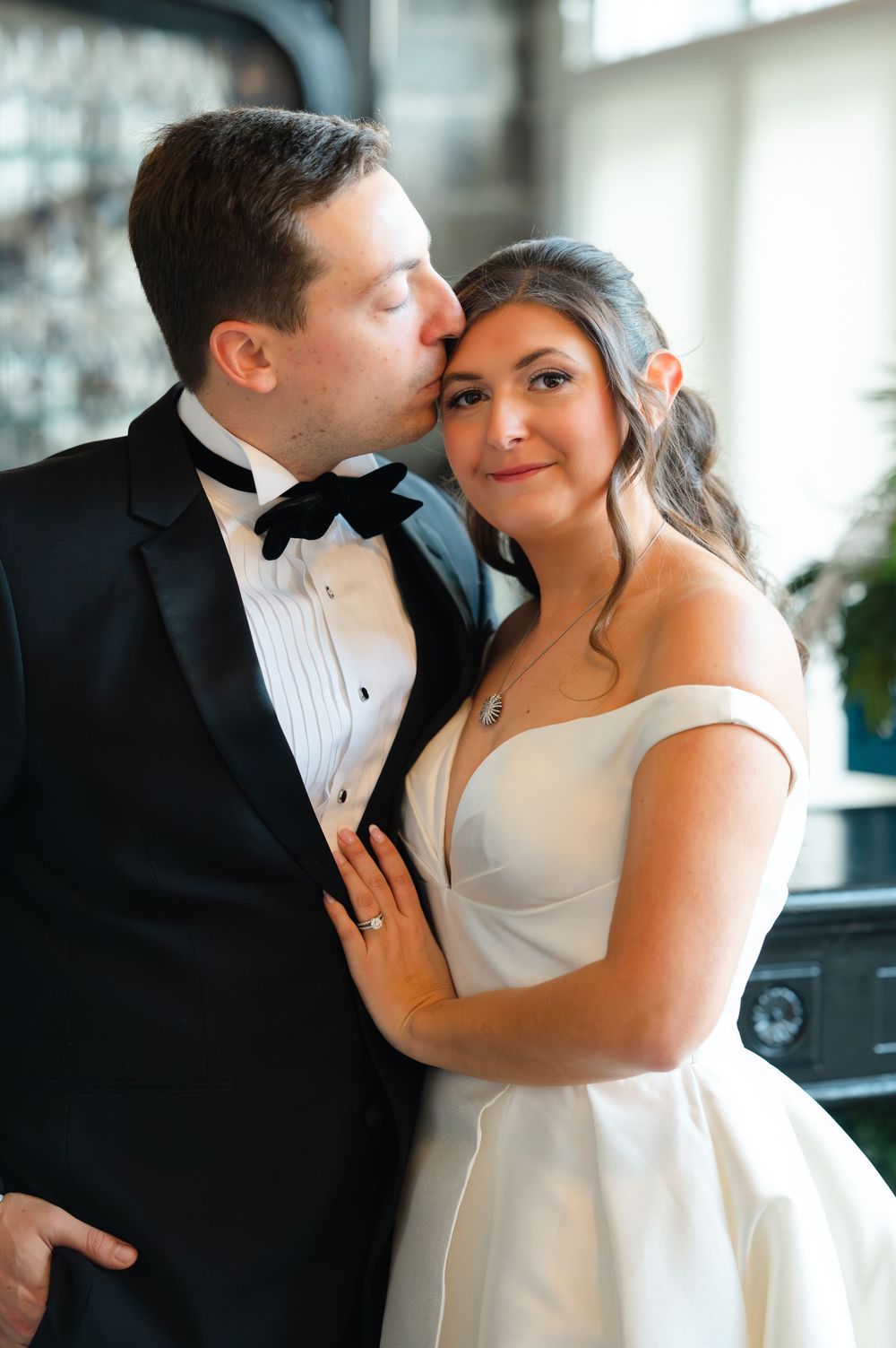 A romantic moment between newlyweds in formal wedding attire sharing intimate embraces in a bright indoor setting.