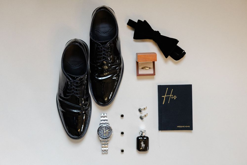 Flat lay collection of men's fashion accessories including black leather shoes, watch, wallet and sunglasses on beige surface.