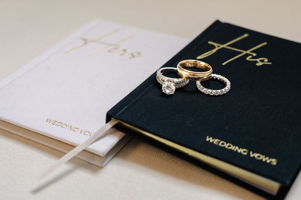 Wedding rings and vows book displayed on dark surface with elegant minimalist styling.